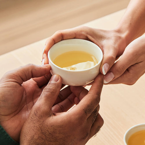 Hände, die sich eine Tasse Tee reichen